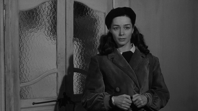 Wide shot frame from Léon Morin, prêtre — standing, door, hat