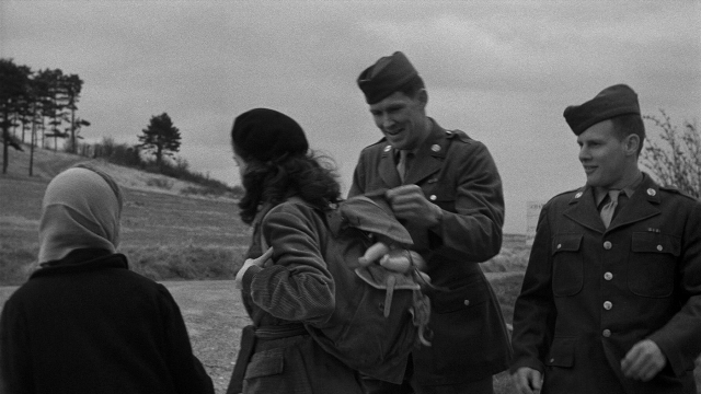 Wide shot frame from Léon Morin, prêtre — standing, dialogue, hat