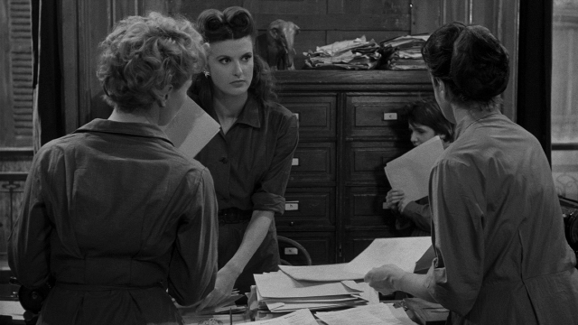Wide shot frame from Léon Morin, prêtre — standing, room, dialogue