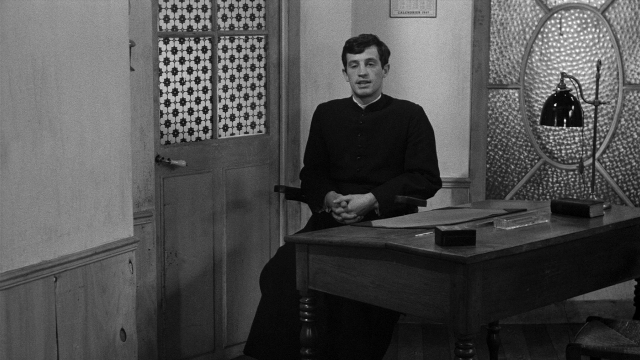 Wide shot frame from Léon Morin, prêtre — sitting, room, table