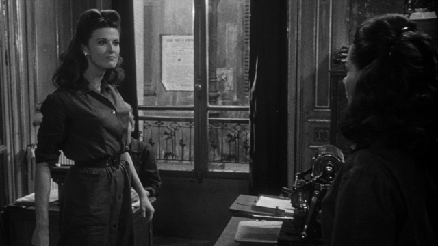 Wide shot frame from Léon Morin, prêtre — standing, room, dress