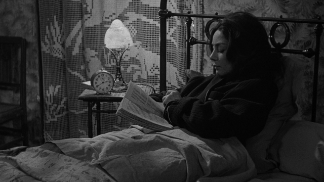 Frame from Léon Morin, prêtre — sitting, book, bed