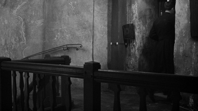 Wide shot frame from Léon Morin, prêtre — standing, room, hat