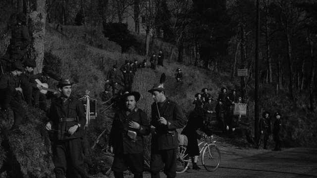 Wide shot frame from Léon Morin, prêtre — walking, street, bicycle