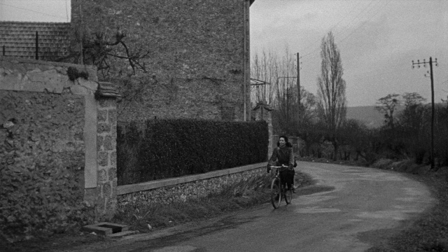 Wide shot frame from Léon Morin, prêtre — street, house, bicycle