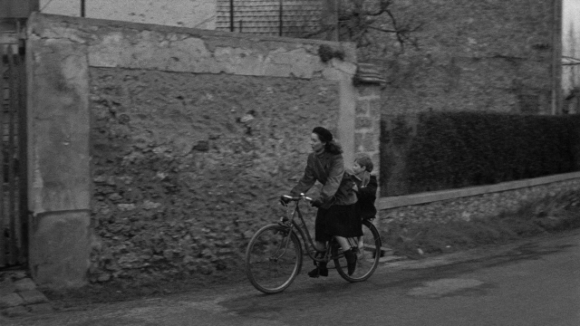 Wide shot frame from Léon Morin, prêtre — street, hat, coat