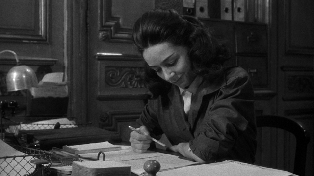 Wide shot frame from Léon Morin, prêtre — sitting, office, face