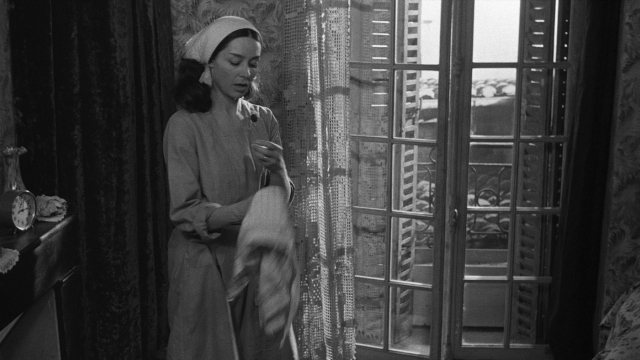 Wide shot frame from Léon Morin, prêtre — standing, room, bed