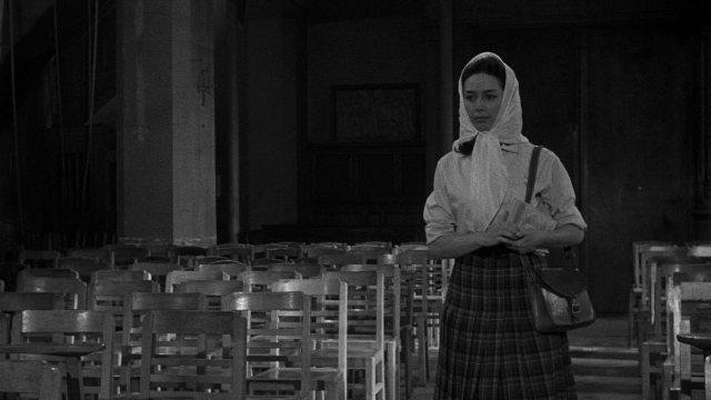 Close-up frame from Léon Morin, prêtre — standing, face, bag