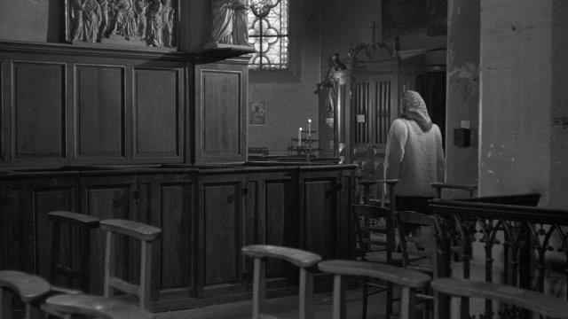 Wide shot frame from Léon Morin, prêtre — standing, room, coat