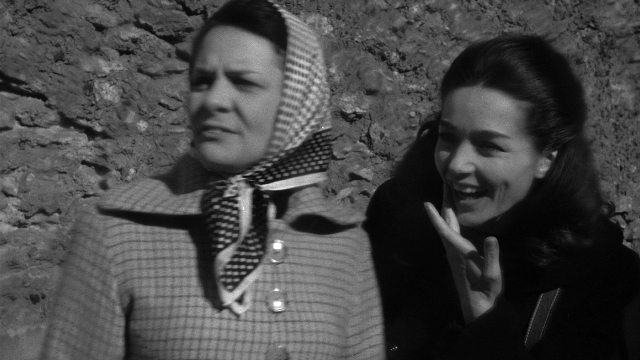 Medium shot frame from Léon Morin, prêtre — standing, coat, hand