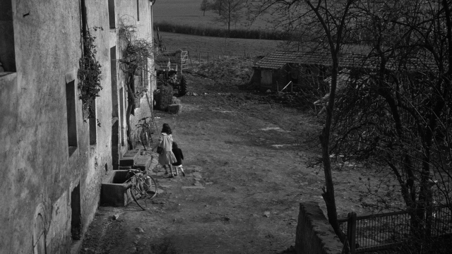 Wide shot frame from Léon Morin, prêtre — walking, house, bicycle