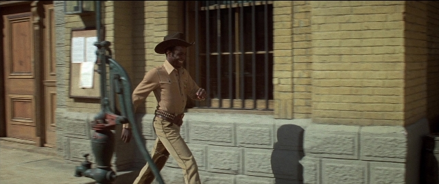 Medium shot frame from Blazing Saddles — walking, door, street