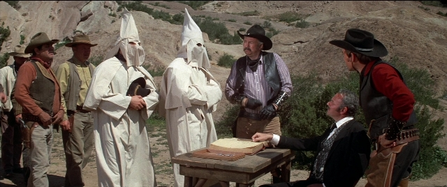Wide shot frame from Blazing Saddles — sitting, book, standing