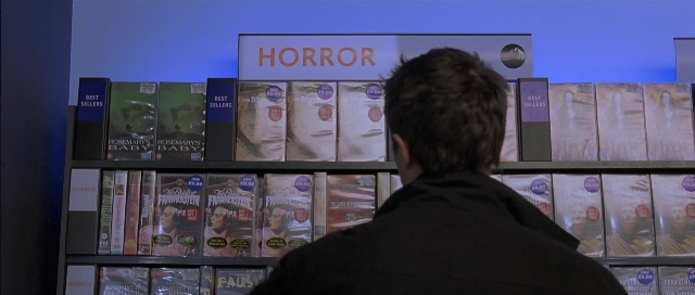 Wide shot frame from About a Boy — standing, bookcase, person