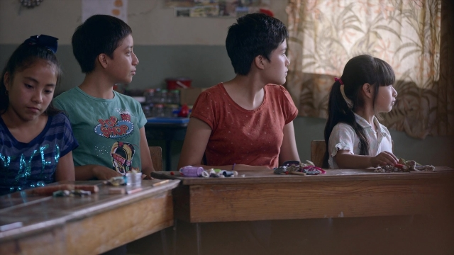 Wide shot frame from Noche de Fuego — sitting, room, table
