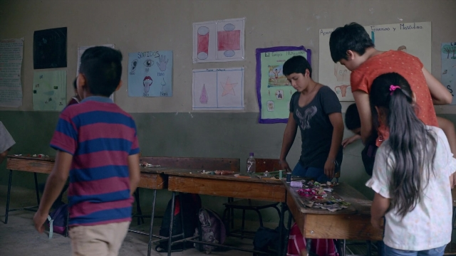 Wide shot frame from Noche de Fuego — standing, room, table