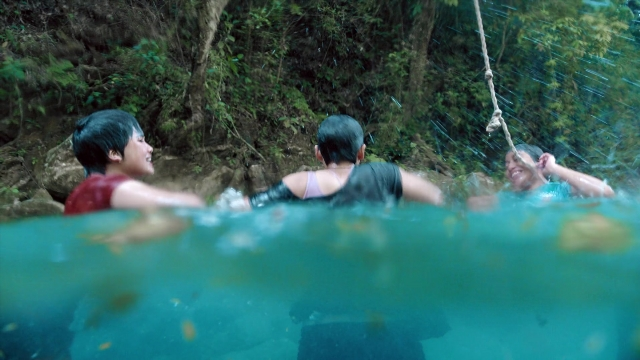 Wide shot frame from Noche de Fuego — water, forest, person