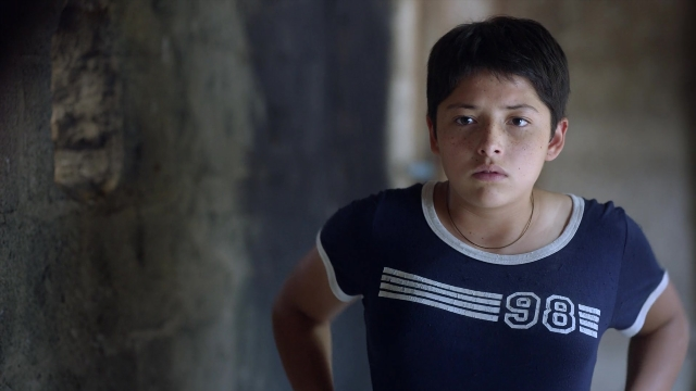 Medium shot frame from Noche de Fuego — standing, room, shirt