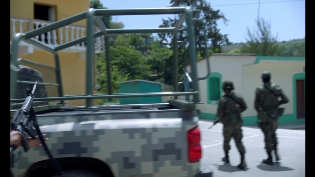 Wide shot frame from Noche de Fuego — walking, street, gun