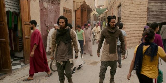 Wide shot frame from Men in Black International — walking, street, beard