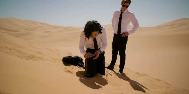 Wide shot frame from Men in Black International — standing, phone, tie