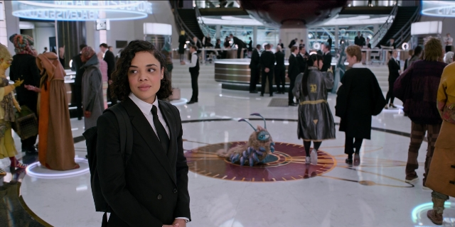 Wide shot frame from Men in Black International — sitting, standing, room