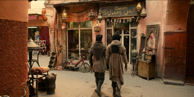 Wide shot frame from Men in Black International — walking, table, door
