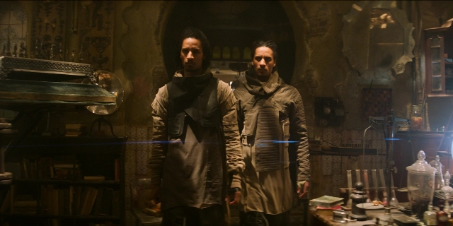 Wide shot frame from Men in Black International — standing, room, table