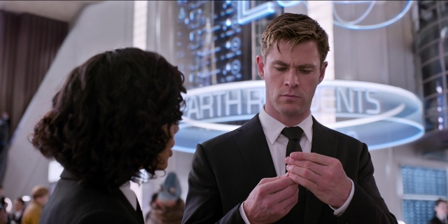 Wide shot frame from Men in Black International — standing, suit, tie