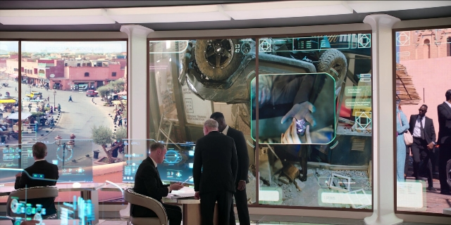Wide shot frame from Men in Black International — sitting, standing, table