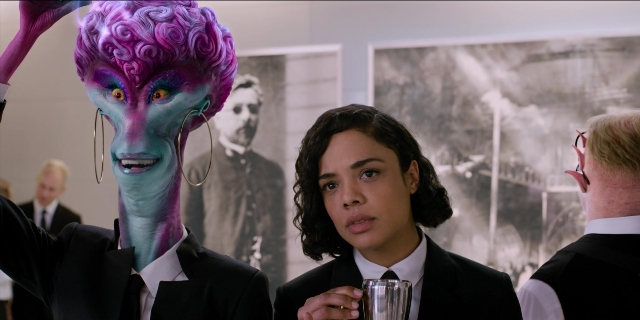 Wide shot frame from Men in Black International — standing, room, suit