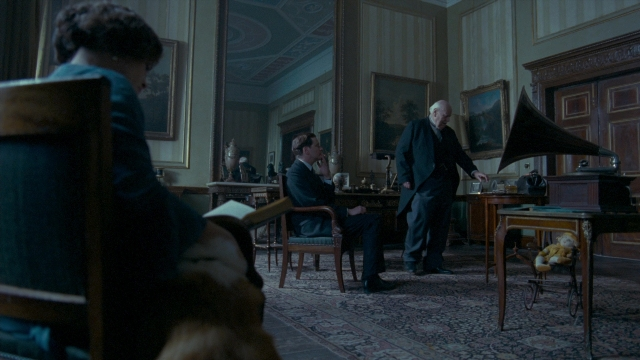 Wide shot frame from The King's Speech — sitting, book, standing