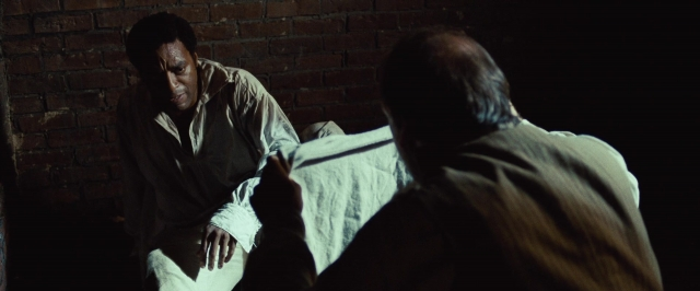 Wide shot frame from 12 Years a Slave — sitting, room, bed
