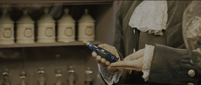 Wide shot frame from Perfume: The Story of a Murderer — hand, bottle, face