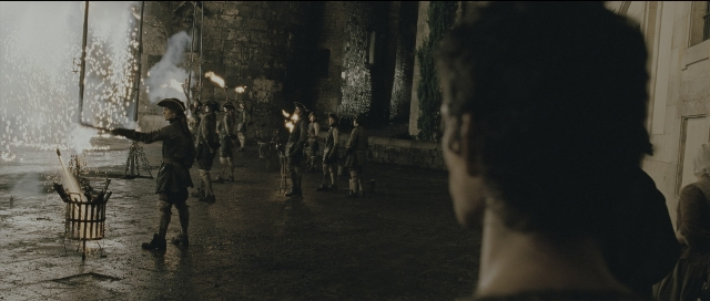 Wide shot frame from Perfume: The Story of a Murderer — standing, hat, fire