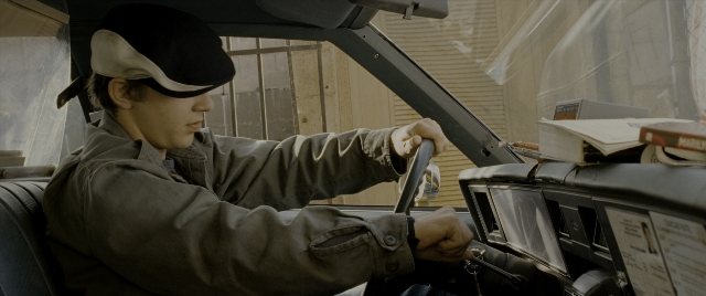 Medium shot frame from Constantine — sitting, hat, car