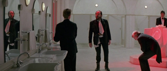 Wide shot frame from The Cook, the Thief, His Wife & Her Lover — dialogue, suit, bathroom