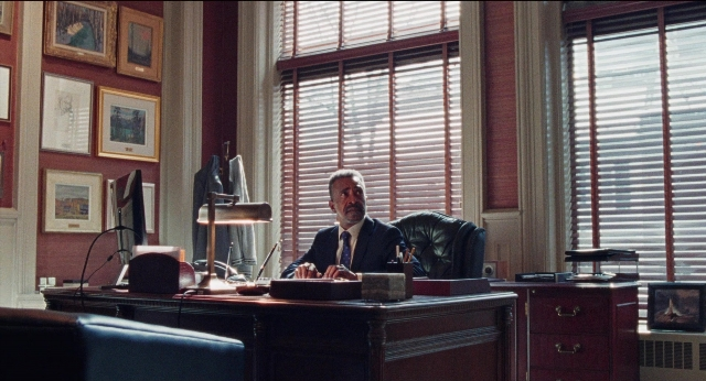 Wide shot frame from Dream Scenario — sitting, desk, room