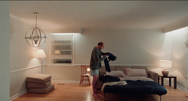 Wide shot frame from Dream Scenario — standing, table, bed