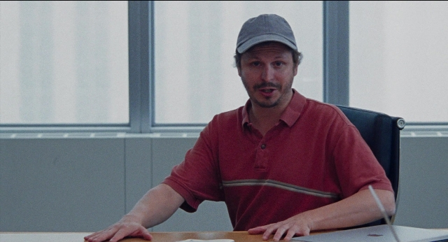 Wide shot frame from Dream Scenario — sitting, hat, shirt