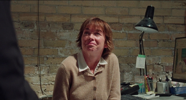 Wide shot frame from Dream Scenario — sitting, phone, office