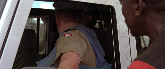 Wide shot frame from Hotel Rwanda — sitting, standing, hat