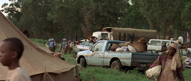 Wide shot frame from Hotel Rwanda — standing, car, tent