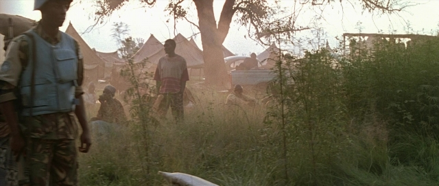Wide shot frame from Hotel Rwanda — sitting, standing, hat