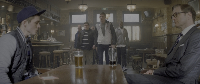 Wide shot frame from Kingsman: The Secret Service — sitting, standing, table