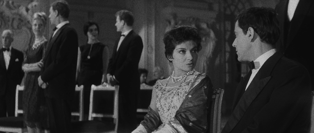 Wide shot frame from L'année dernière à Marienbad — sitting, room, suit