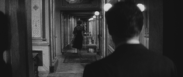 Wide shot frame from L'année dernière à Marienbad — standing, hat, coat