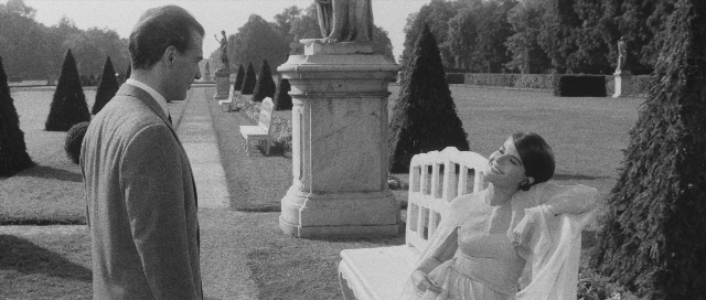Medium shot frame from L'année dernière à Marienbad — sitting, standing, suit