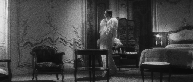 Wide shot frame from L'année dernière à Marienbad — standing, room, table